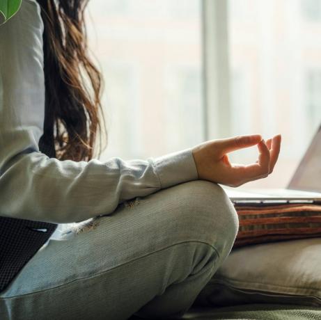 seorang wanita Asia paruh baya dengan celana jeans biru duduk di tempat tidur dalam pose yoga di depan laptop bekerja jarak jauh di rumah belanja online di masa karantina