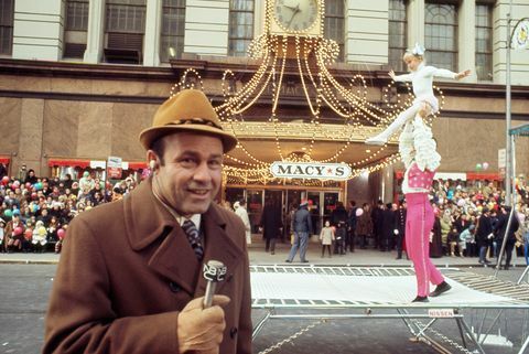 joe garagiola berbicara ke mikrofon dengan akrobat di latar belakang pada parade hari thanksgiving macy pada tahun 1970