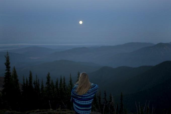 wanita terbungkus selimut melihat lanskap pegunungan dengan bulan purnama, tampilan belakang