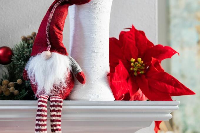 dekorasi kurcaci Natal liburan norweigan klasik duduk di atas mantel modern berwarna putih dengan vas putih dengan kayu putih dan bunga poinsettia