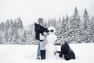 keluarga tiga orang membangun manusia salju di salju