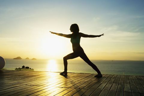 Wanita melakukan yoga di tepi laut saat matahari terbenam