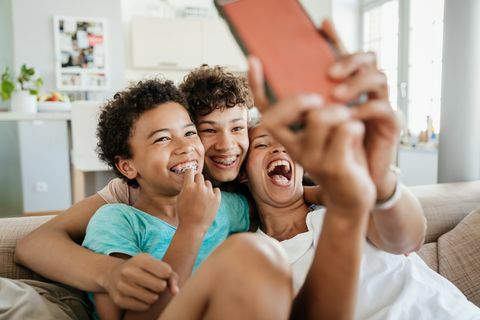 seorang ibu tunggal bersenang-senang dengan kedua putranya di rumah, duduk di sofa mengambil selfie di smartphone-nya