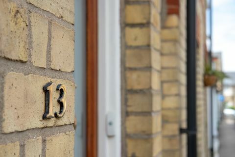 Tampilan fokus dangkal dari nomor kuningan 13 terlihat terpasang di pintu masuk rumah bertingkat yang terbuat dari batu bata di kota pasar Inggris ini