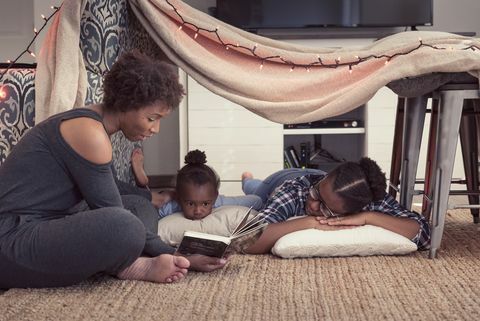 ibu duduk sampai benteng yang terbuat dari selimut bersama kedua putrinya, membaca cerita dari sebuah buku