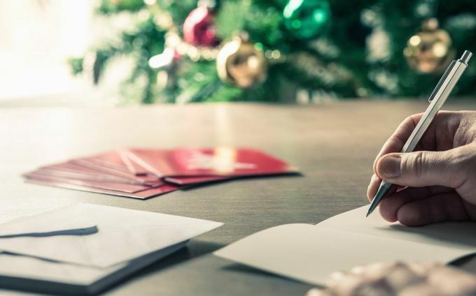 menulis pesan kartu Natal di depan pohon liburan