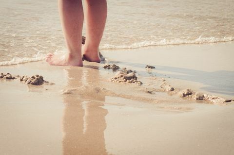 Menutup kaki wanita di tangan di pantai - laut masuk