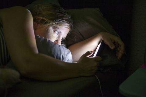 Wanita melihat ponsel pintar di tempat tidur