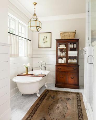 kamar mandi dengan lemari linen kayu antik dan bak mandi berkaki putih