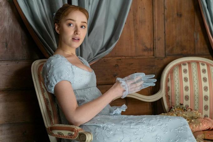 phoebe dynevor sebagai daphne bridgerton di episode 102, duduk, mengenakan gaun berpinggang kekaisaran berwarna biru