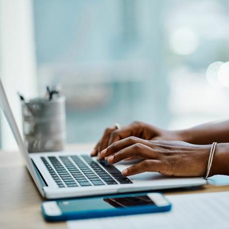 tampilan jarak dekat dari seorang pengusaha wanita kulit hitam yang mengetik pada keyboard laptop di kantor sendirian