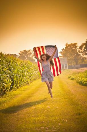 gadis petani remaja berlari melalui lapangan melambaikan bendera kami