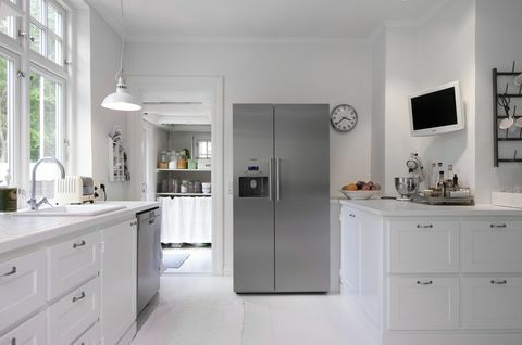 Dapur putih dengan kulkas perak tegak di renovasi rumah Hanne Davidsen, Silkesborg, Denmark.