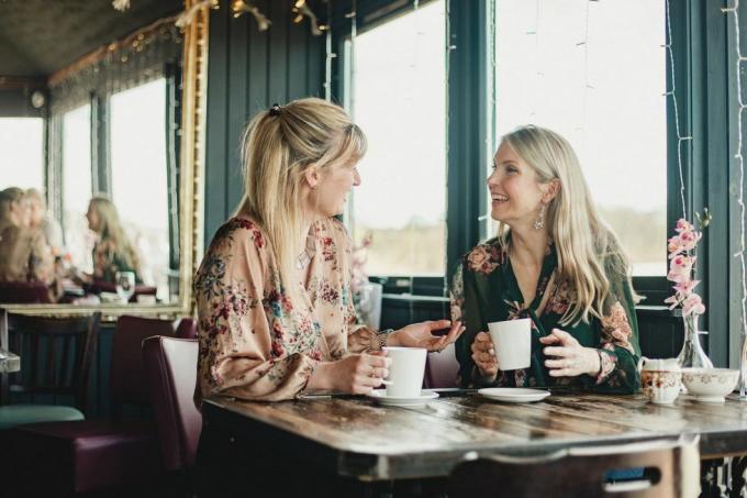 bidikan tampak depan dari dua wanita paruh baya yang cantik sedang menikmati kopi bersama di kafe, mereka duduk di meja dan tertawa bersama