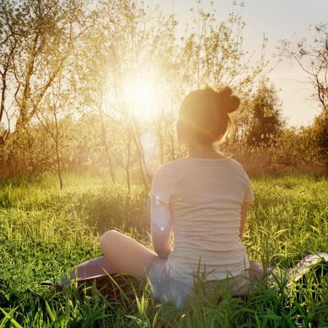 wanita muda duduk dalam posisi yoga menikmati matahari terbenam di alam