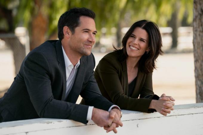 dua karakter yang merupakan mantan suami istri dalam serial tersebut, bersandar di dinding luar ruangan, tersenyum, berbicara