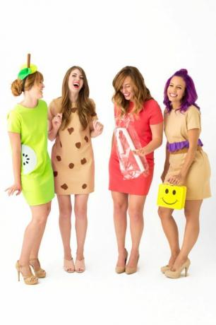 empat wanita tertawa dalam gaun pendek berpakaian sebagai "wanita makan siang," satu membawa kotak makan siang wajah tersenyum kuning