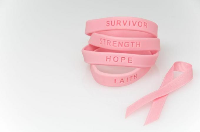 tumpukan gelang karet merah muda bertuliskan selamat, kekuatan, harapan, iman dan pita merah muda di sebelahnya